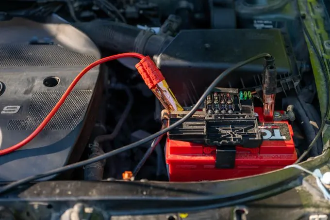 Car battery with jumper cables in an engine bay